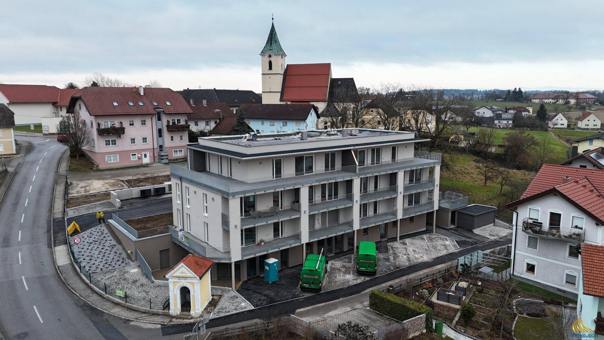 Luftaufnahme eines modernen Mehrfamilienhauses in ländlicher Umgebung mit Kirche im Hintergrund.