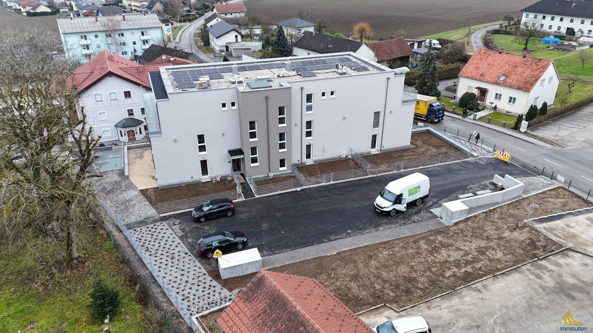 Moderne Gebäudefassade eines Neubaus mit Parkplätzen und umliegenden Wohnhäusern.
