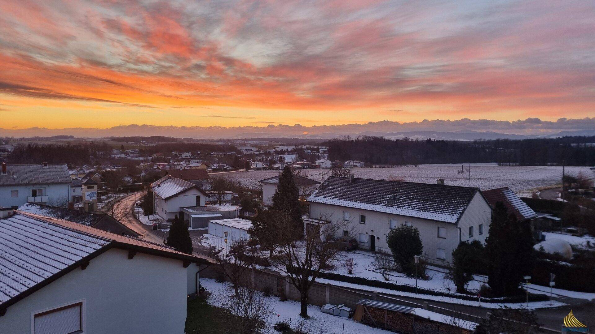 Weitläufige Winterlandschaft bei Sonnenuntergang mit ländlicher Bebauung und dramatischem Himmel.