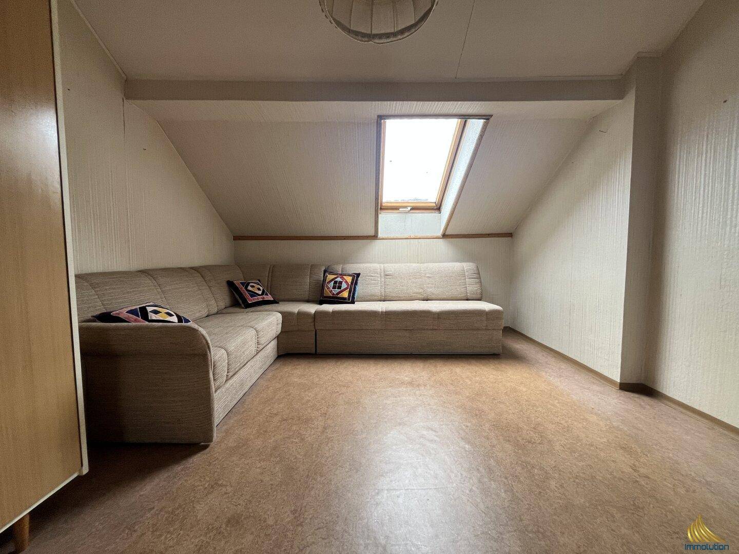 Gemütlicher Wohnbereich im Dachgeschoss mit Schrägen, Sofa und Dachfenster.
