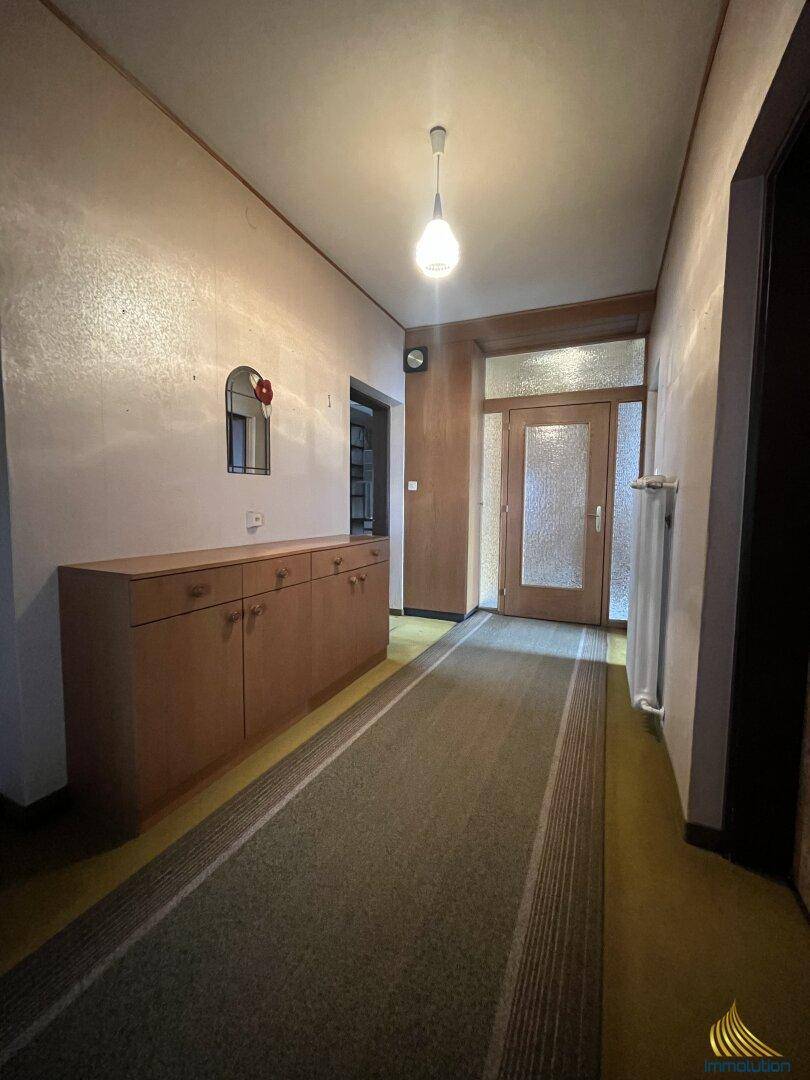 Langer Flur mit Holzmöbeln, Teppichläufer und einer Eingangstür mit Glaseinsatz.
