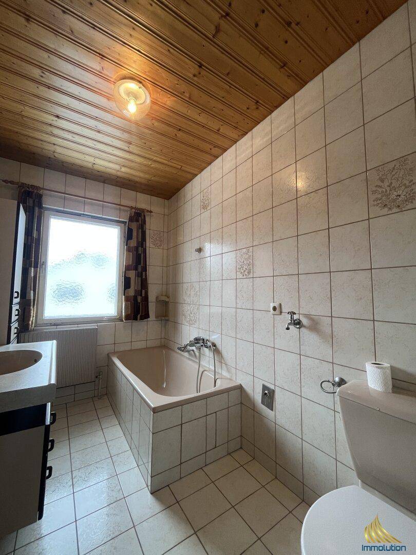 Badezimmer mit Badewanne, WC und Holzdecke, gefliest in hellem Beige.