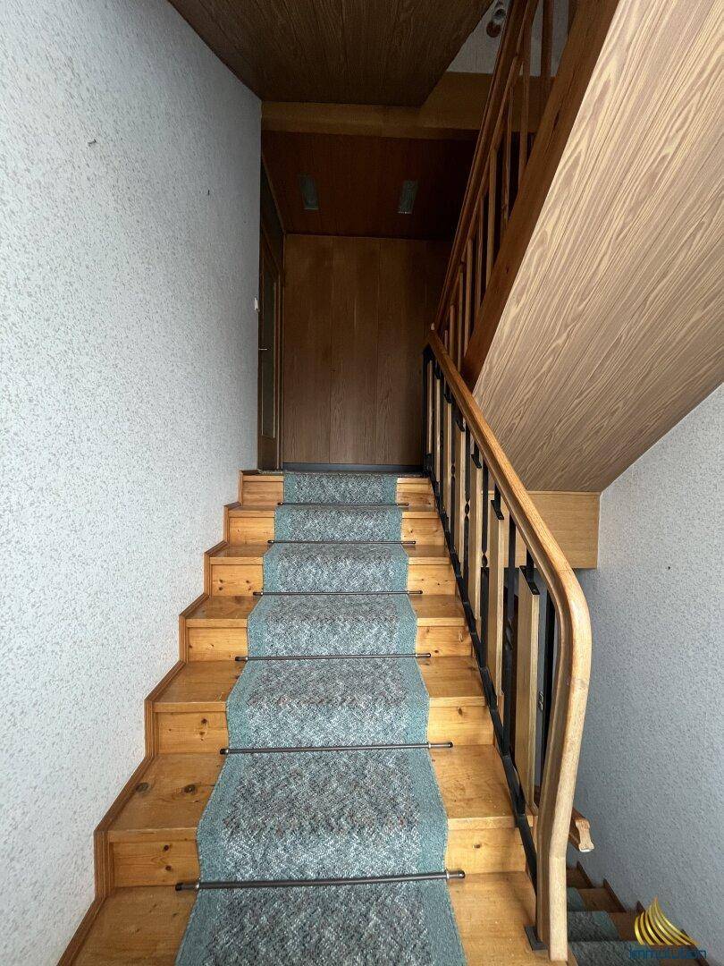 Holztreppe mit Teppichläufer und Geländer, die in die oberen Stockwerke führt.