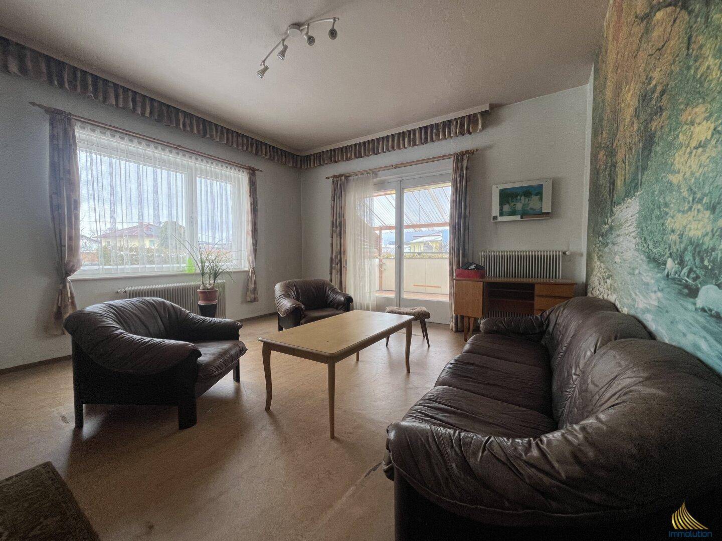 Wohnzimmer mit Ledersofas, einem großen Fenster und Zugang zu einem Balkon.