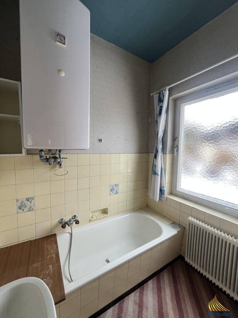 Badezimmer mit Badewanne, Fenster und gelben Fliesen im 80er-Jahre-Stil.