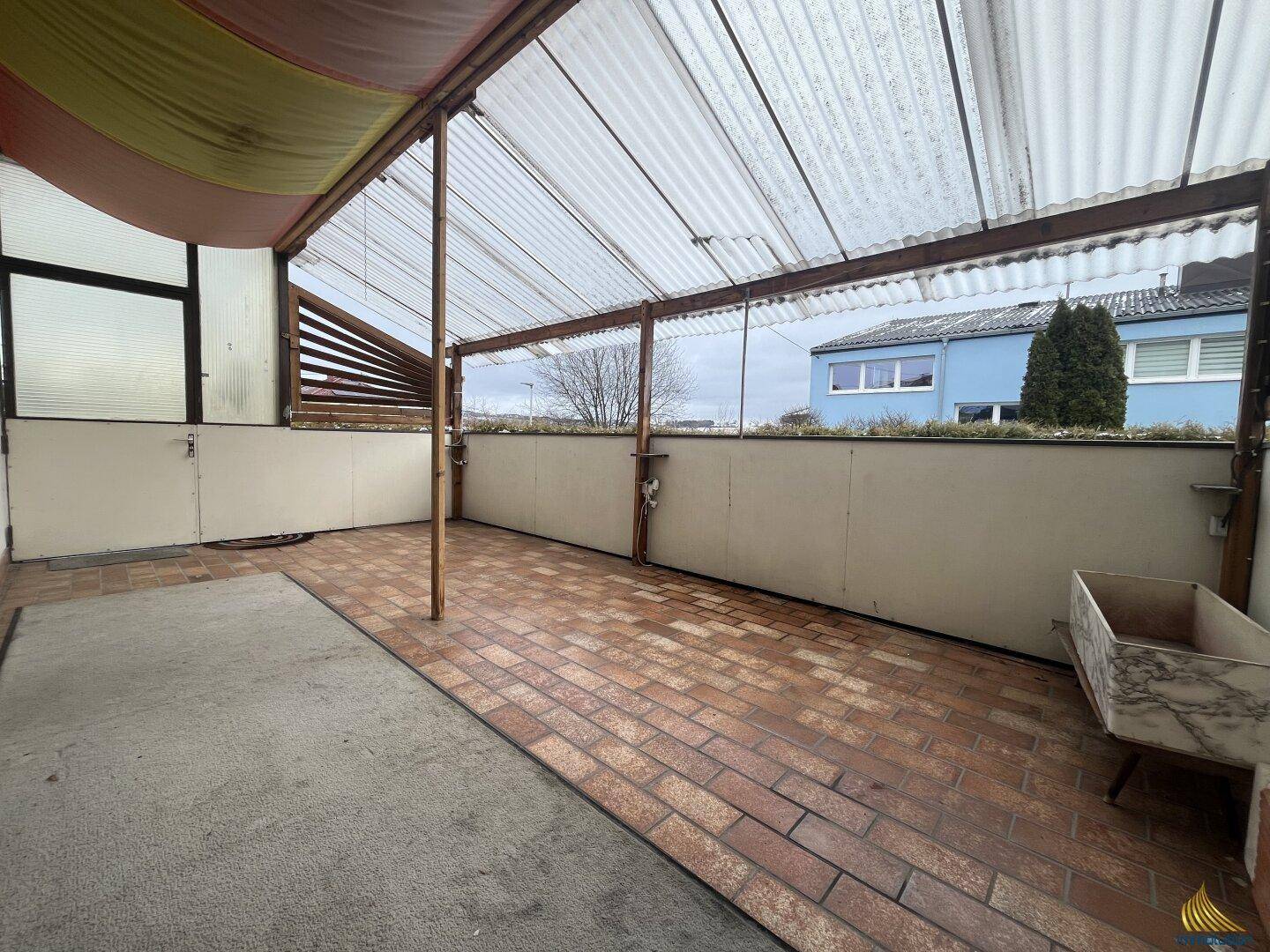 Überdachte Terrasse mit Ziegelboden und Blick auf die Nachbarschaft.