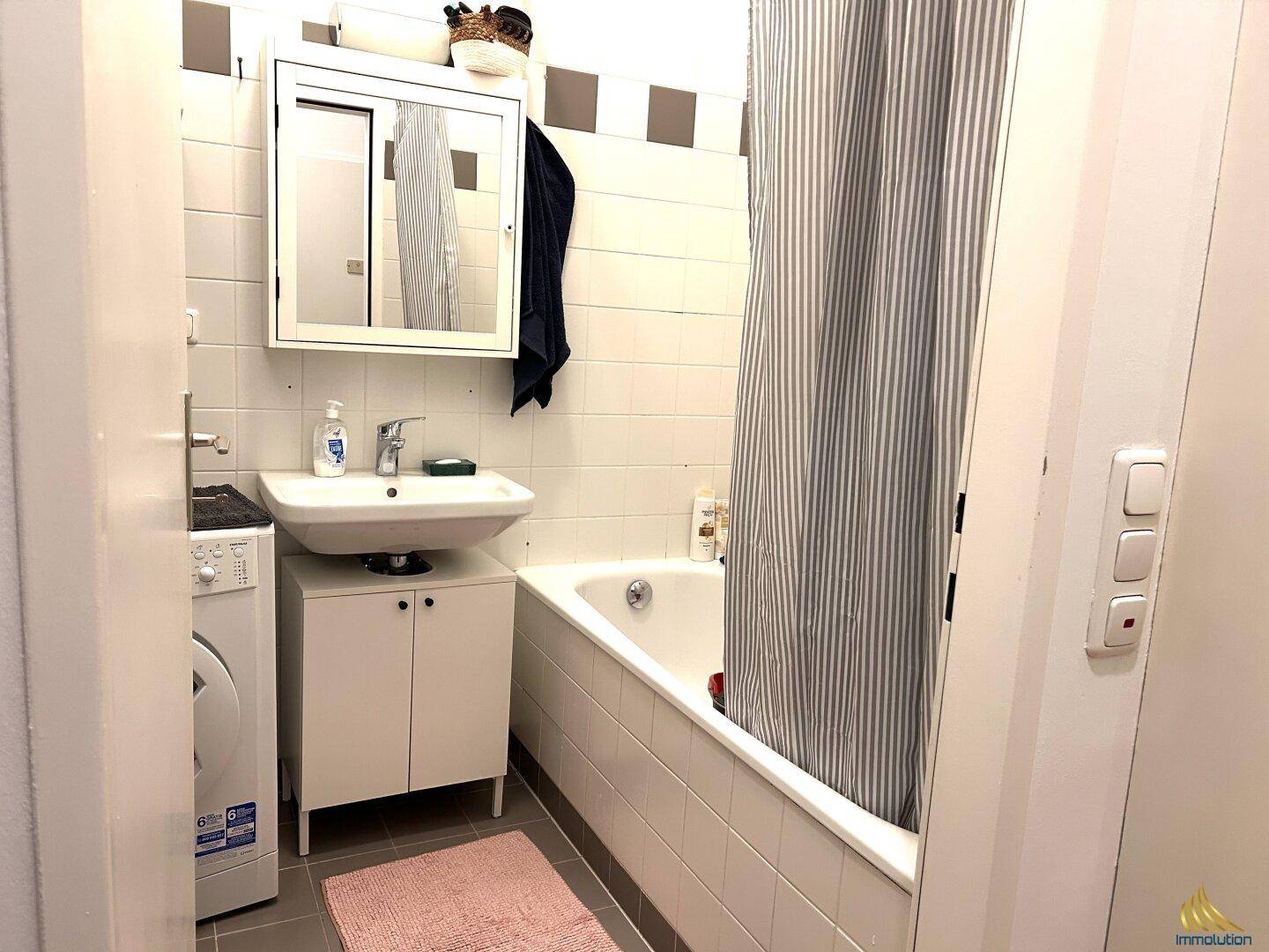 Funktionales Badezimmer mit Badewanne, Waschbecken und Waschmaschine in hellen Fliesen.