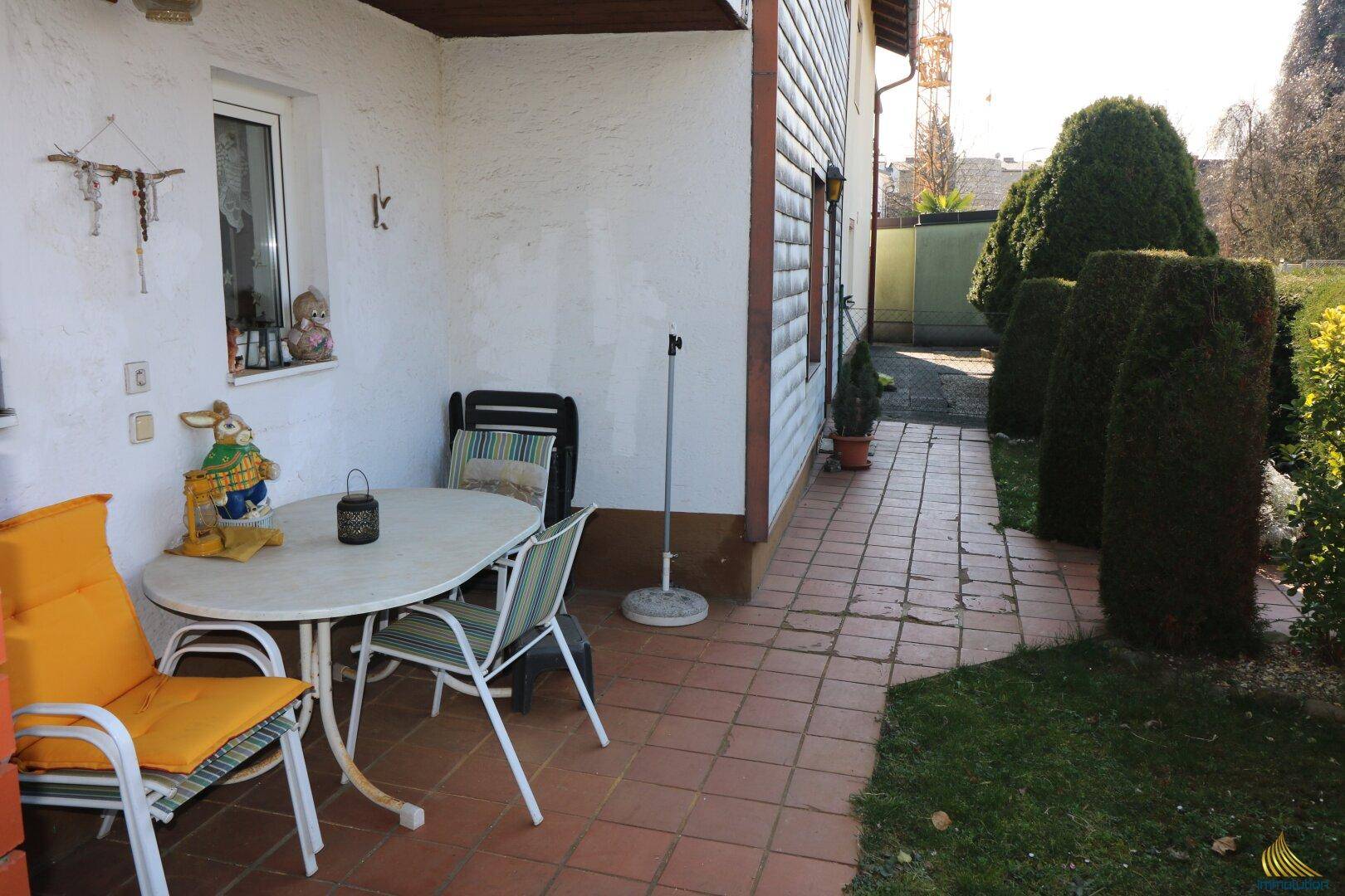 Gemütliche gepflasterte Terrasse mit Gartenmöbeln und Zugang zum grünen Gartenbereich.