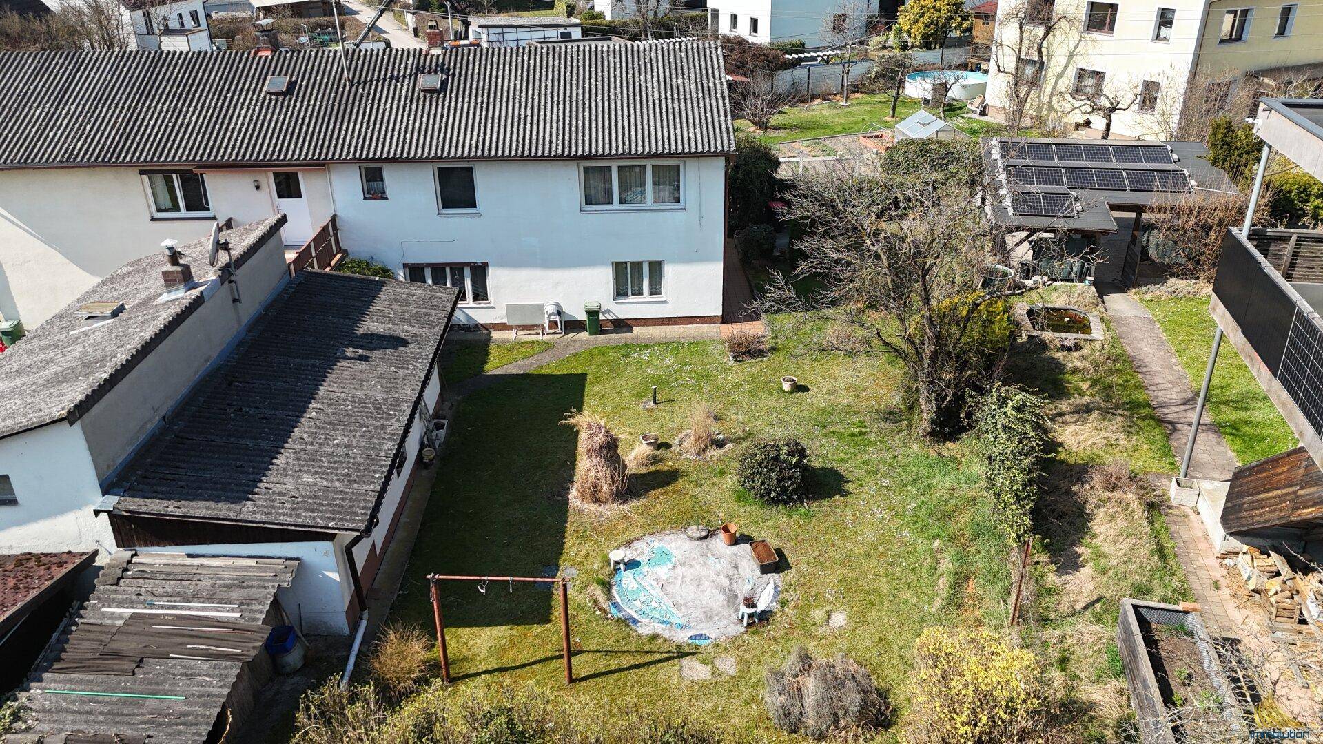 Luftaufnahme des Anwesens mit großem Garten, Nebengebäuden und umliegender Bebauung.