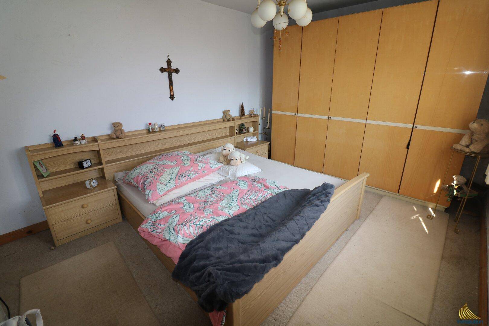 Schlafzimmer mit Doppelbett, hellen Holzschränken und Teppichboden, gut beleuchtet.