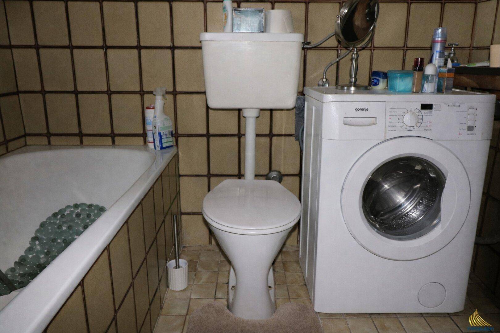 Badezimmer mit Badewanne, Toilette und Waschmaschine, gefliest in Braun und Beige.