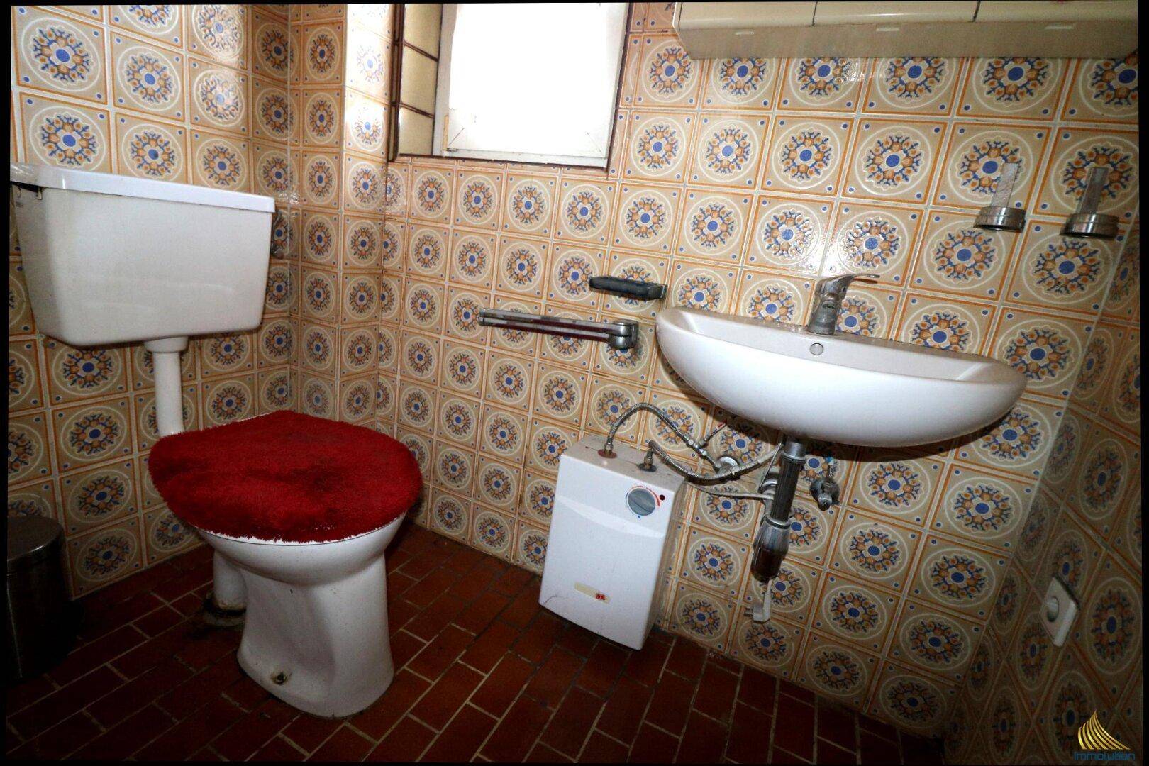 Kleines WC mit gemusterten Fliesen, Toilette, Waschbecken und einem kleinen Fenster.
