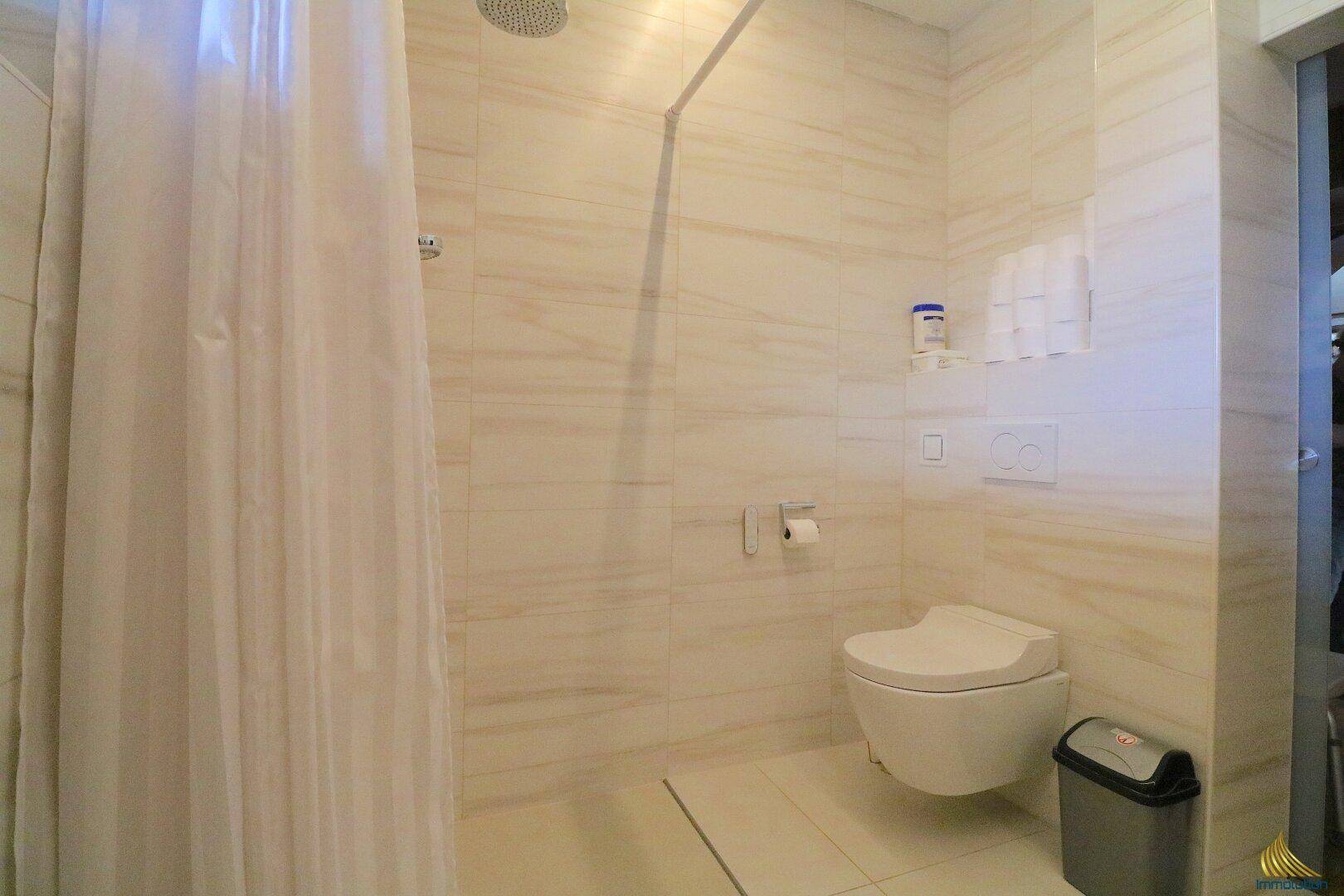 Badezimmer mit wandhängendem WC und geräumiger, ebenerdiger Dusche.