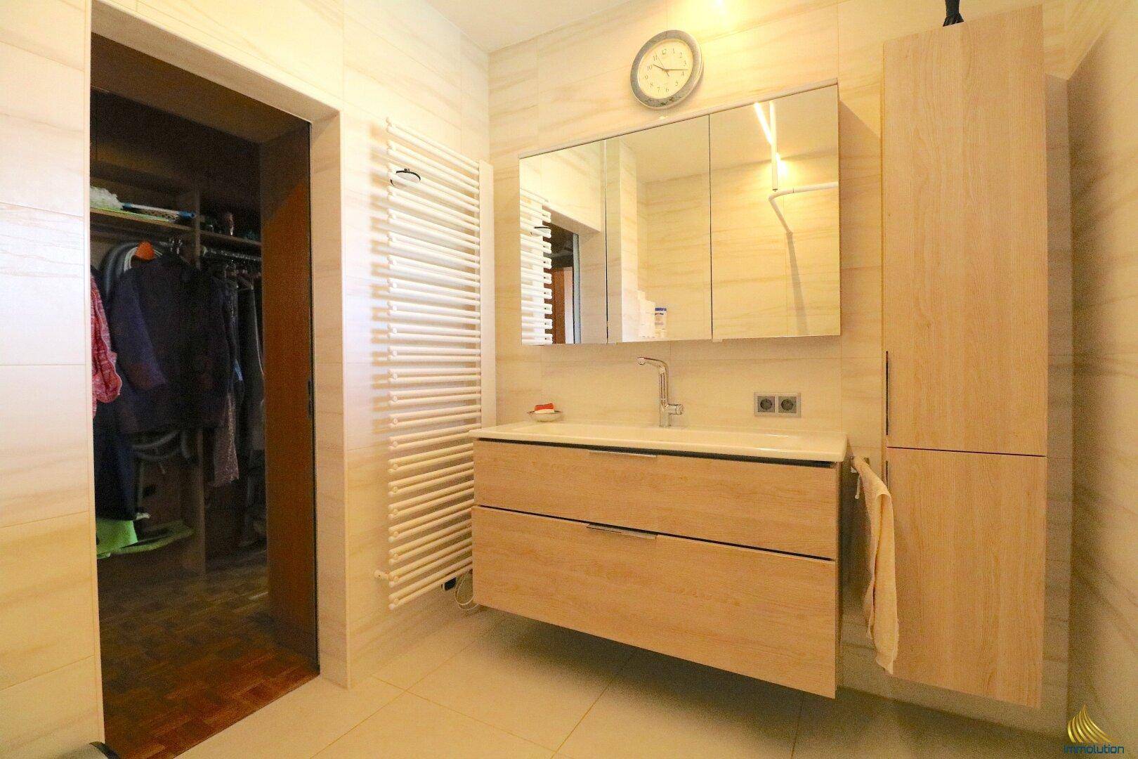 Modernes Badezimmer mit Einzelwaschbecken, Handtuchheizkörper und angrenzendem Ankleidezimmer.