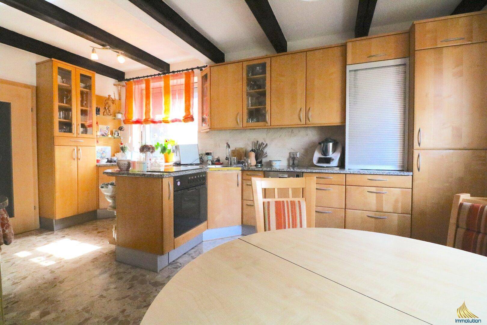 Gemütliche Wohnküche mit Holzelementen, Esstisch und Blick auf die Einbauküche.