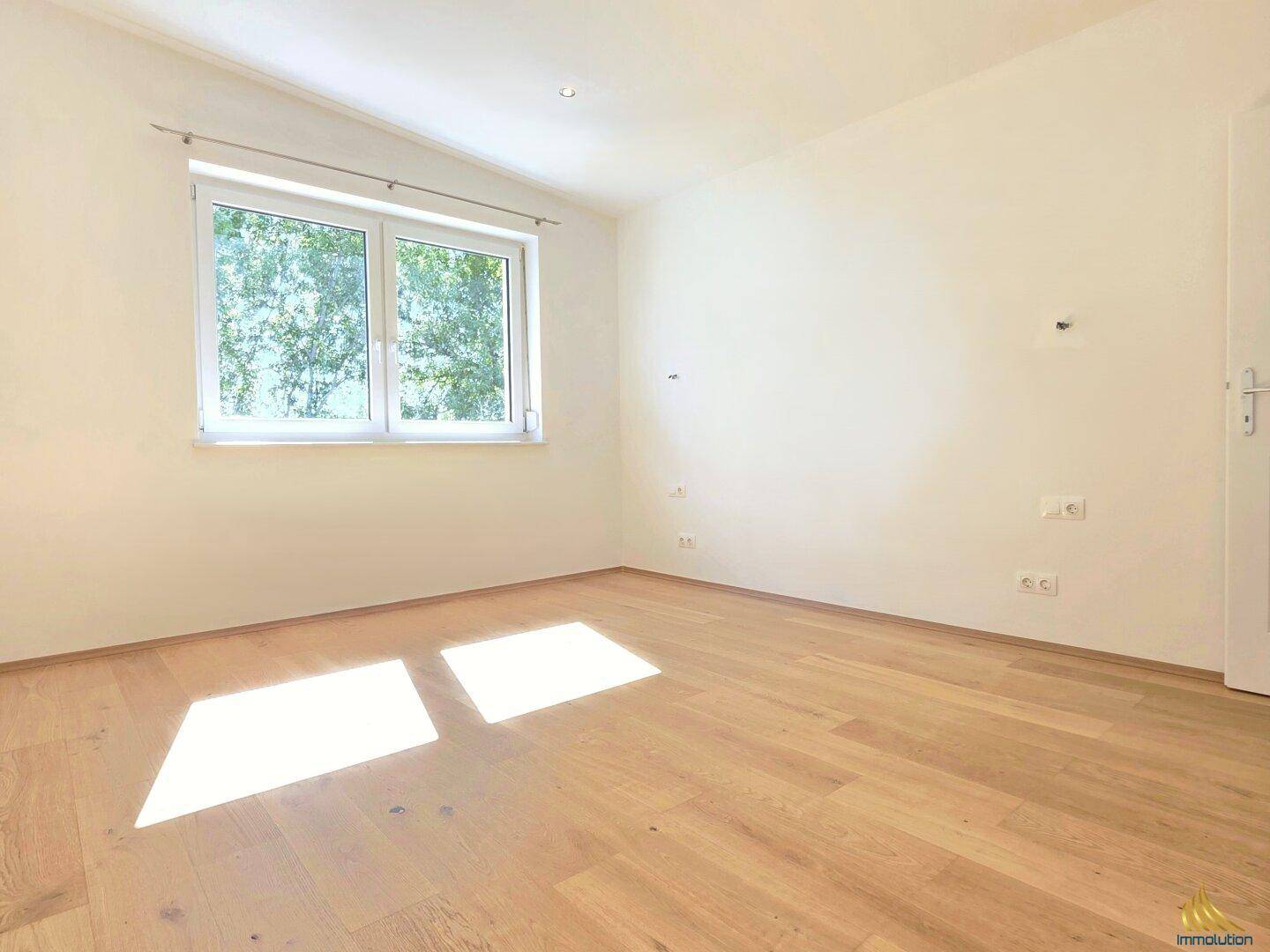 Helles Zimmer mit Holzboden und großem Fenster, das viel natürliches Licht hereinlässt.