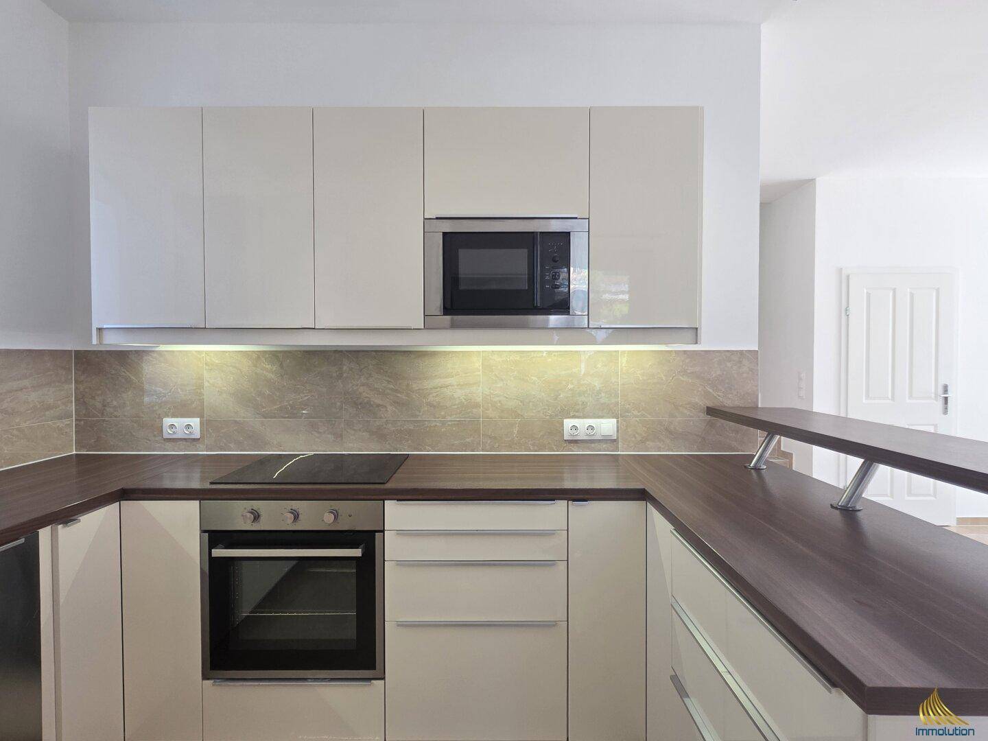 Moderne Einbauküche mit hellen Schränken, Induktionskochfeld und Backofen.