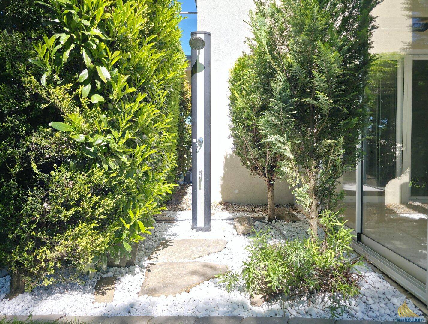 Außenbereich mit einer modernen Gartendusche, umgeben von grünen Pflanzen und Kies.