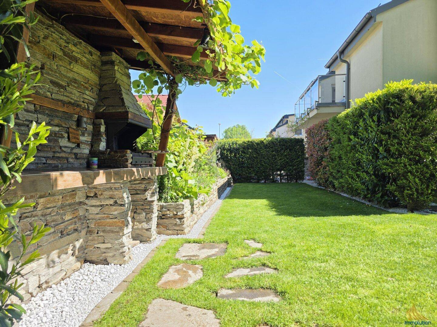 Gepflegter Garten mit gemauertem Grillplatz, Rasenfläche und Hecke.
