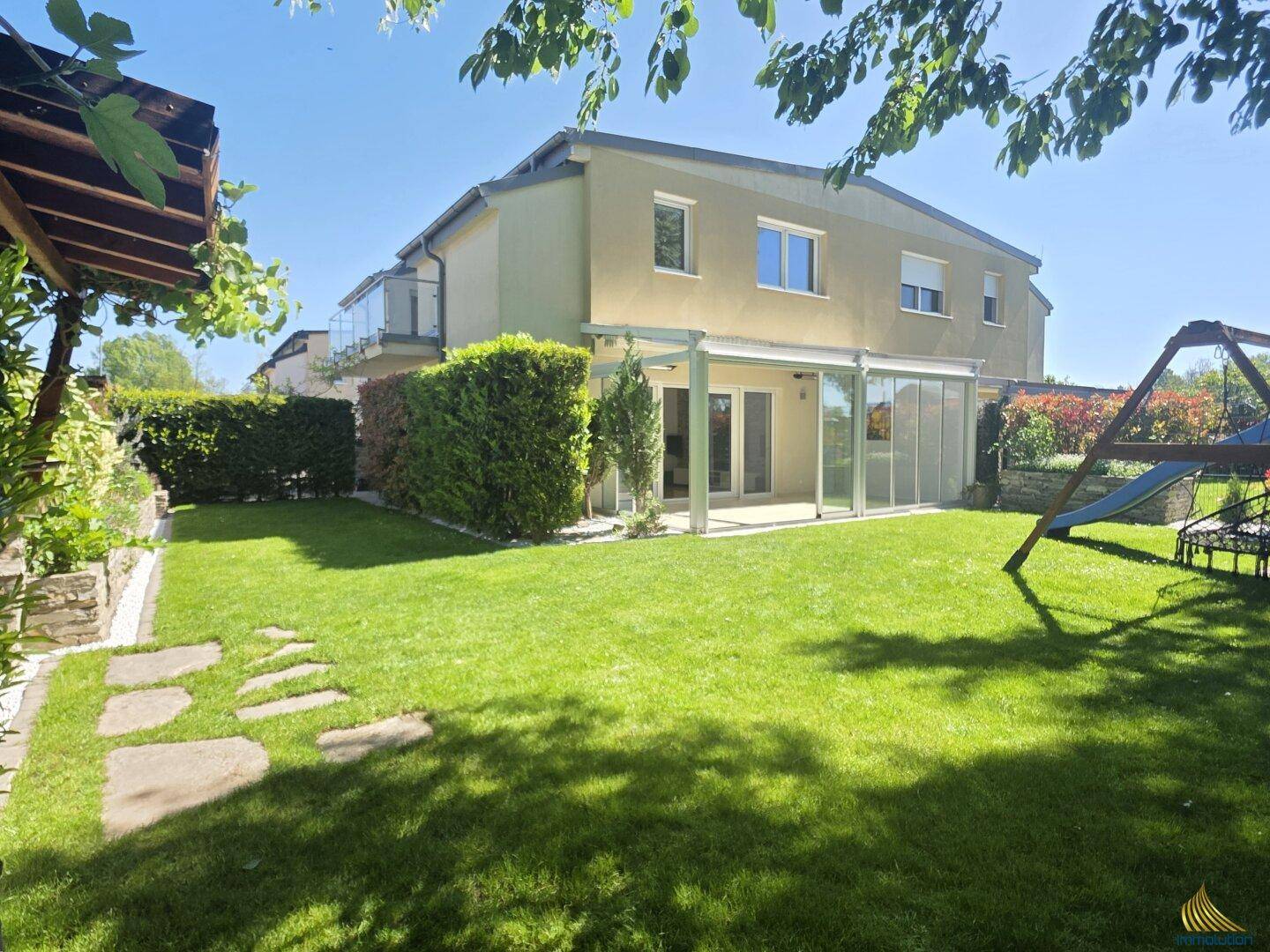 Rückansicht des modernen Hauses mit großem Garten, Rasenfläche und Spielplatz.