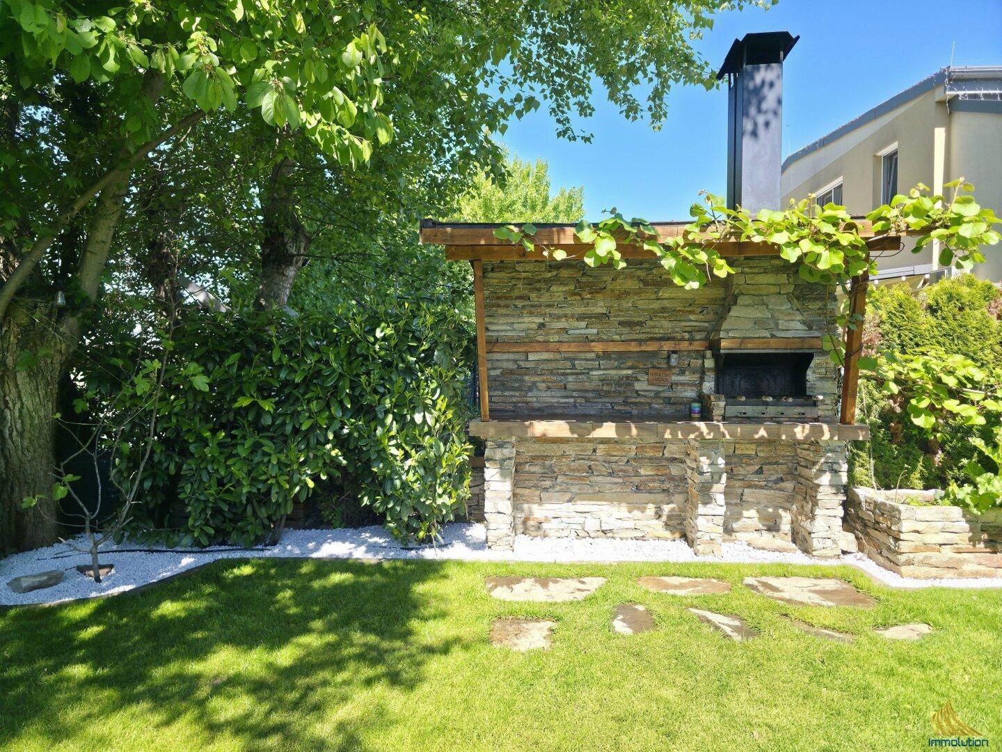 Gemauerter Grillplatz im Garten unter einem Baum mit Rasenfläche.