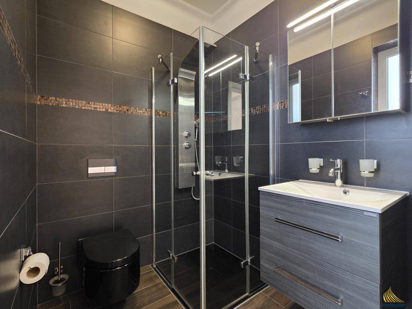 Modernes Badezimmer mit dunklen Fliesen, Duschkabine und schwarzer Toilette.