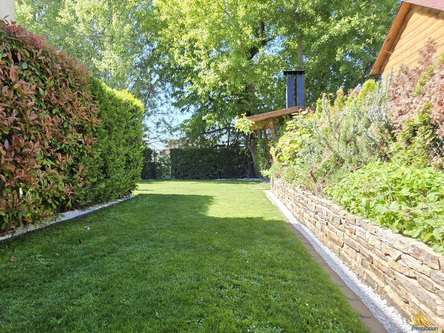 Langer, gepflegter Rasenweg im Garten mit Steinmauer und Hecke.