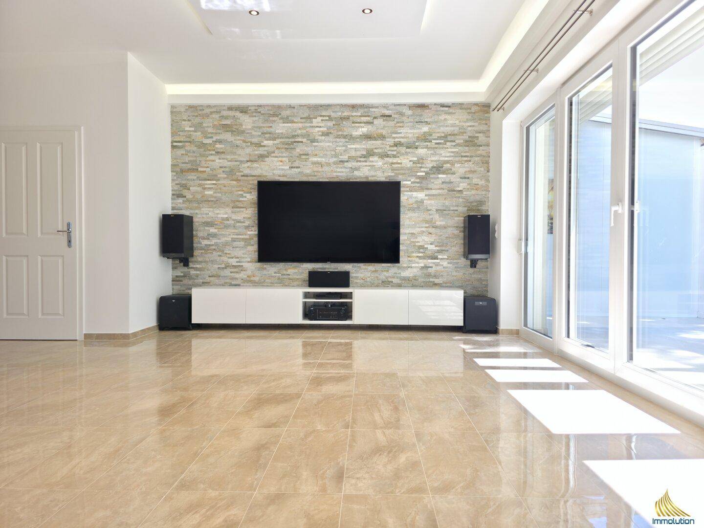 Modernes Wohnzimmer mit Steinwand, TV-Möbel und großen Fensterfronten.