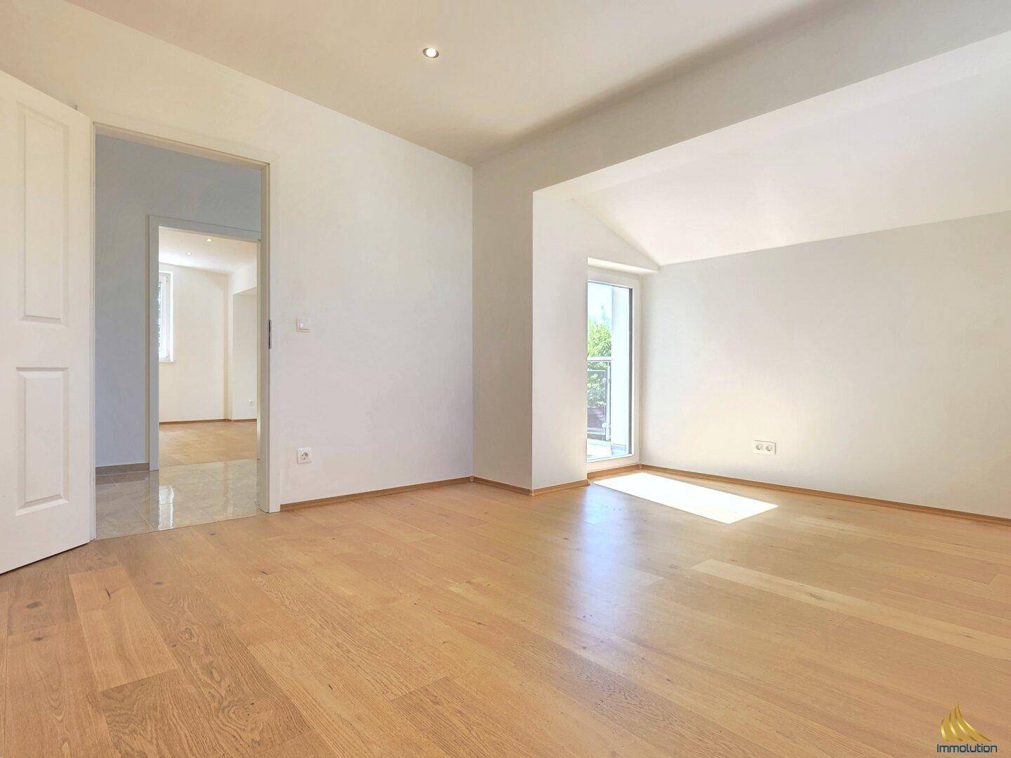 Heller Raum mit Holzboden und Zugang zu einem Balkon oder einer Terrasse.