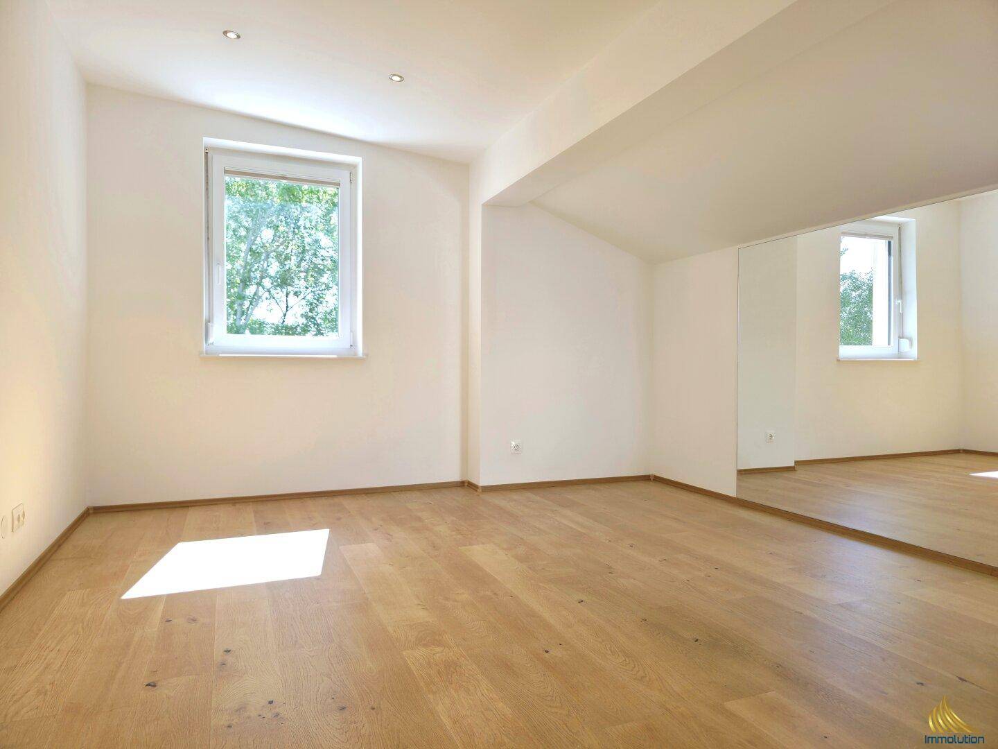 Lichtdurchflutetes Zimmer mit Holzboden und mehreren Fenstern für eine helle Atmosphäre.