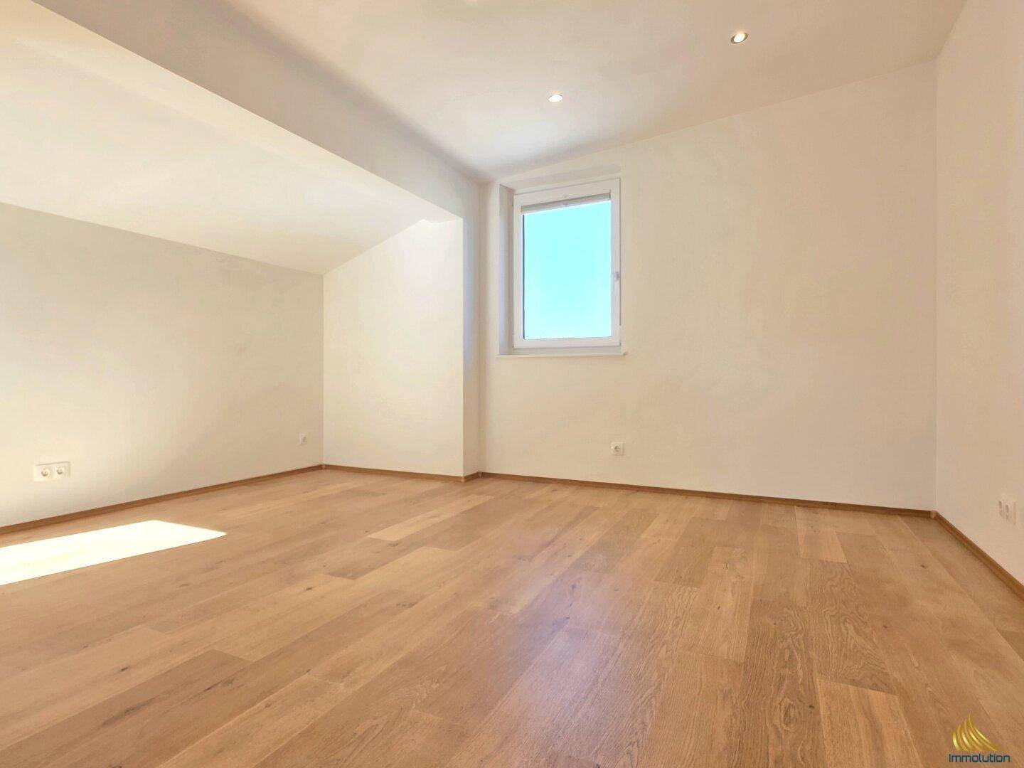 Geräumiges Zimmer mit Holzboden und einem Fenster, das den Raum hell erscheinen lässt.
