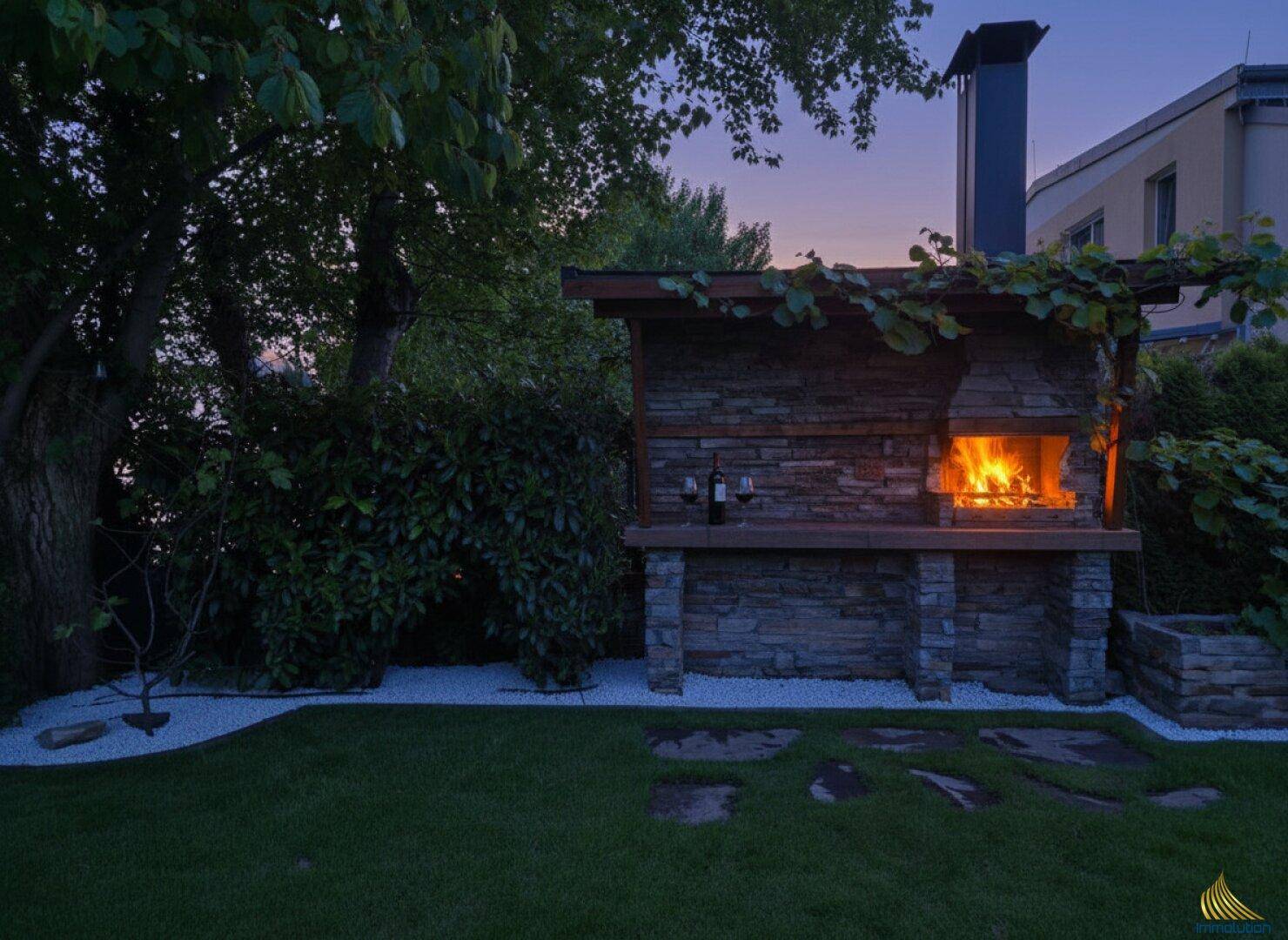 Gemütlicher Grillplatz im Garten bei Sonnenuntergang mit brennendem Feuer.