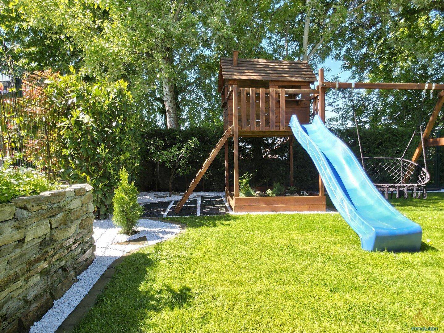 Sonniger Garten mit Kinderspielplatz, Rutsche und Baumhaus.