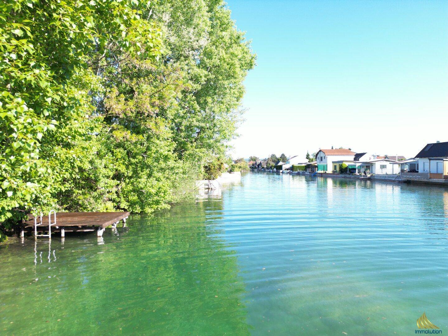 Idyllischer Kanalblick mit üppigem Grün und Häusern am Ufer unter blauem Himmel.