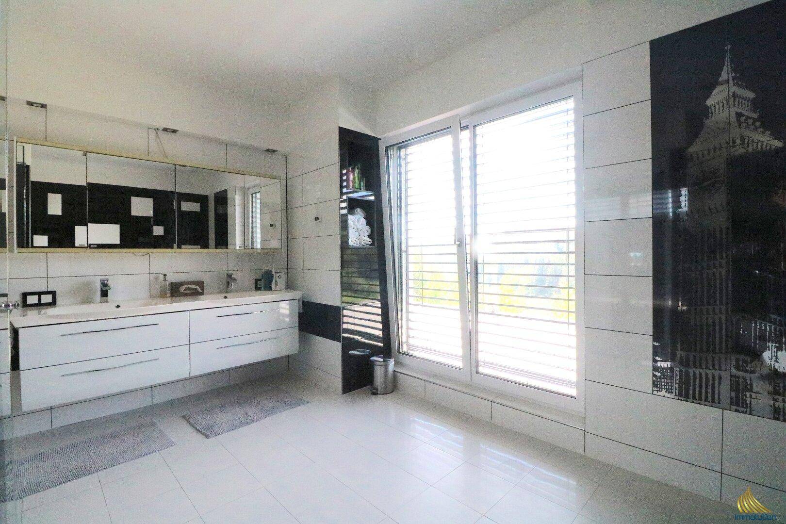 Modernes Badezimmer mit Doppelwaschbecken, großem Spiegelschrank und schwarz-weißen Fliesen.
