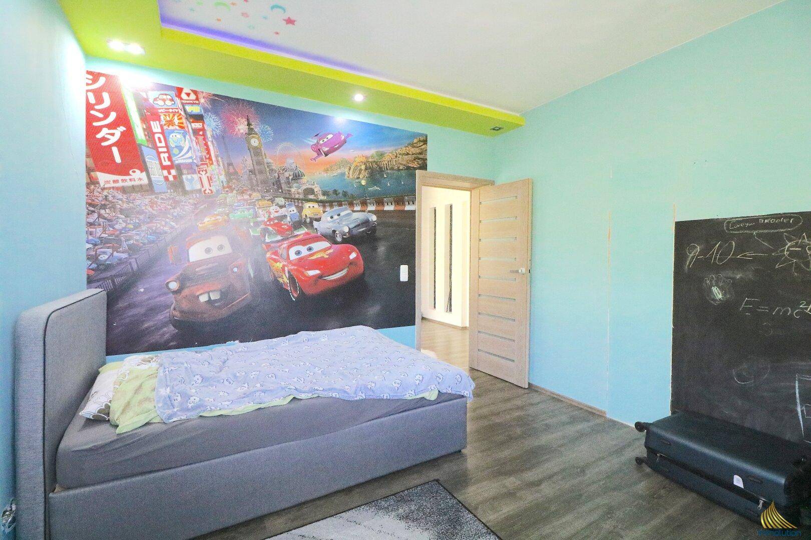 Kinderzimmer mit Bett, großer Wandmalerei mit "Cars"-Motiv und einer Tafel.