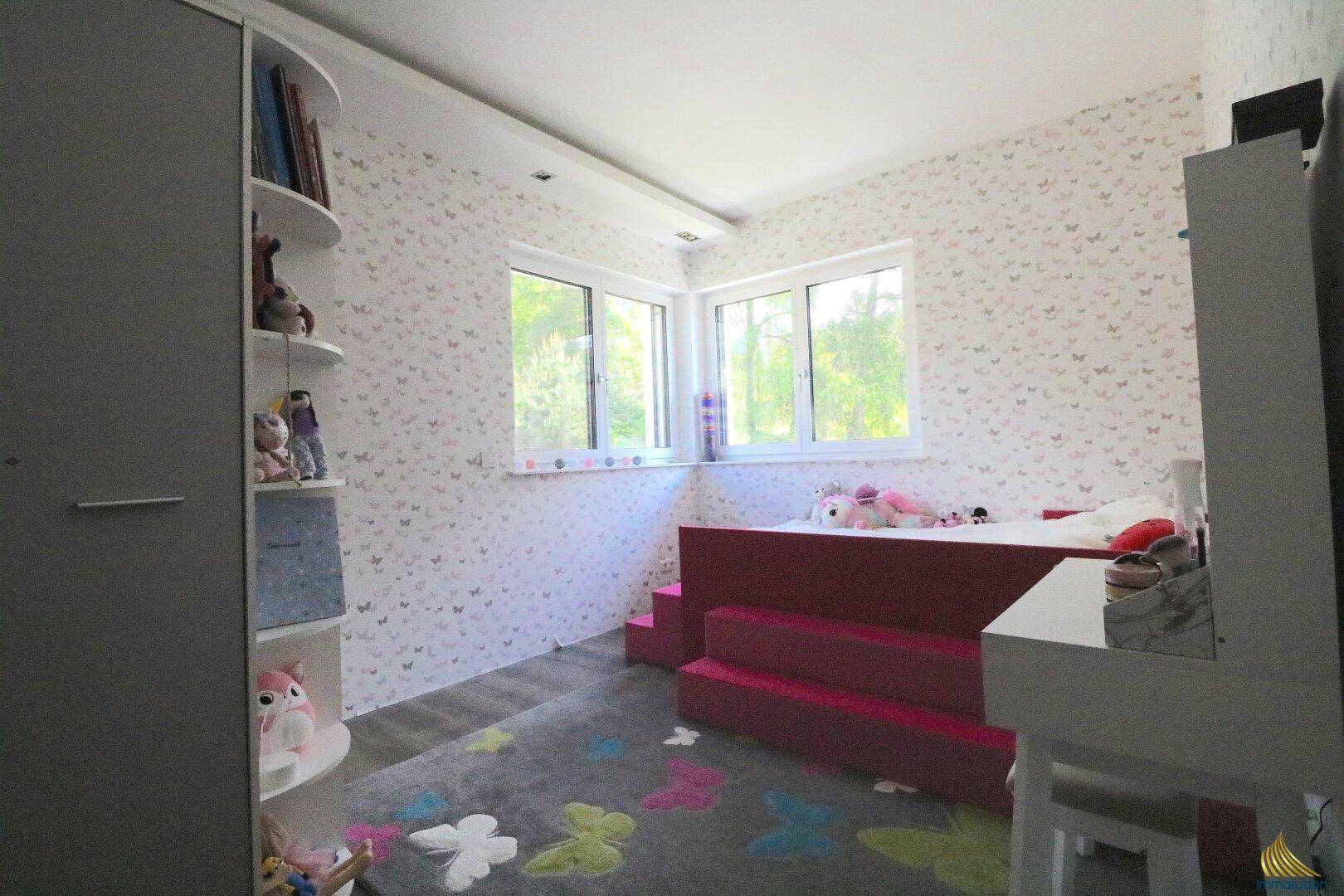 Helles Kinderzimmer mit verspielter Tapete, erhöhtem Bett und Laminatboden.
