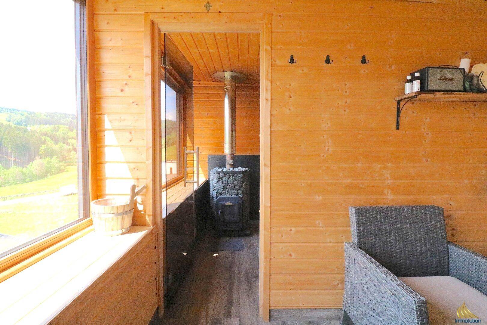 Gemütlicher Holzraum mit Blick in eine Sauna und weitem Ausblick in die Natur.