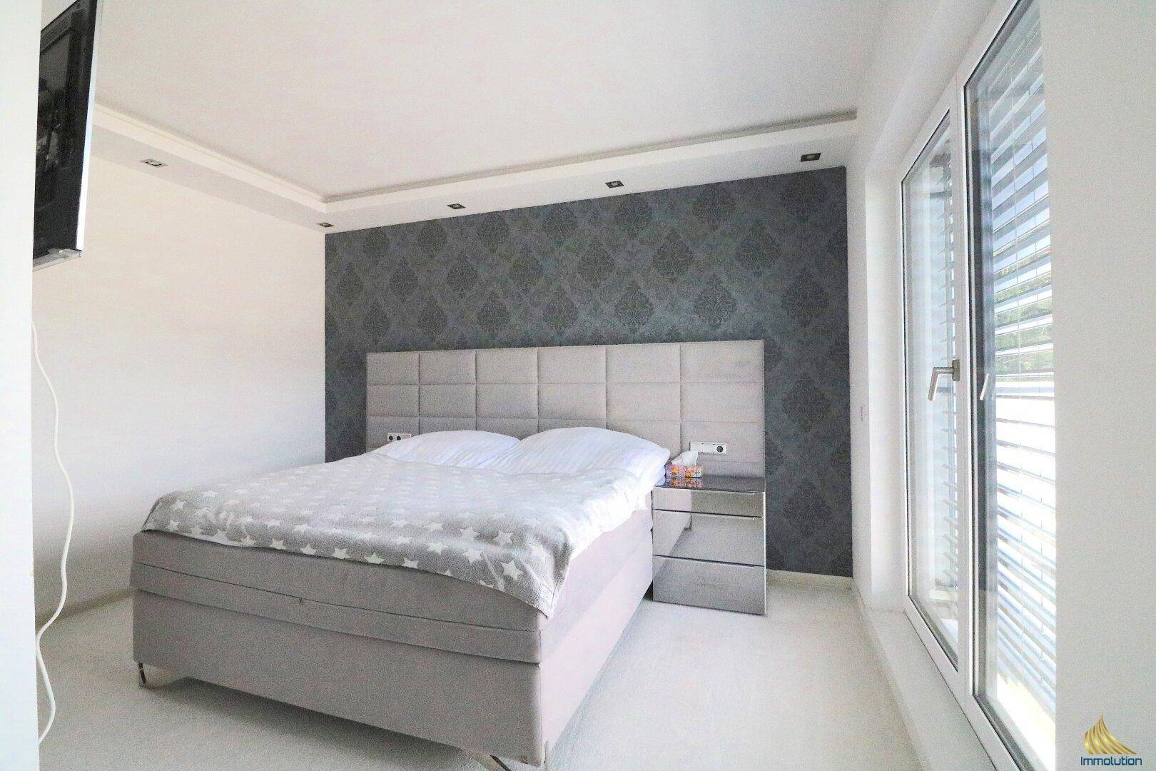 Helles Schlafzimmer mit modernem Bett, stilvoller Tapetenwand und großem Fenster.