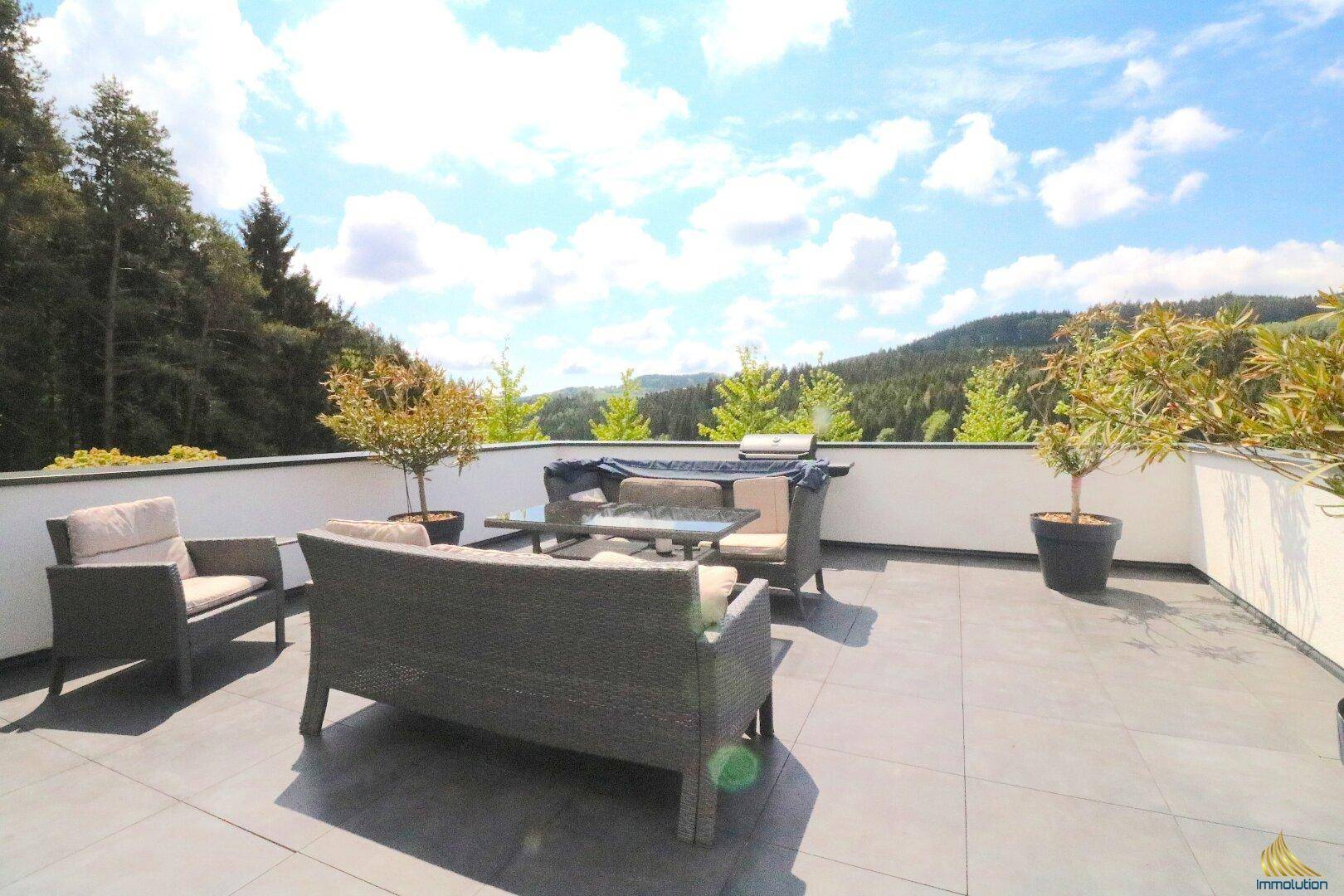 Große Sonnenterrasse mit modernen Loungemöbeln, Fliesenboden und weitem Blick über die Hügellandschaft.