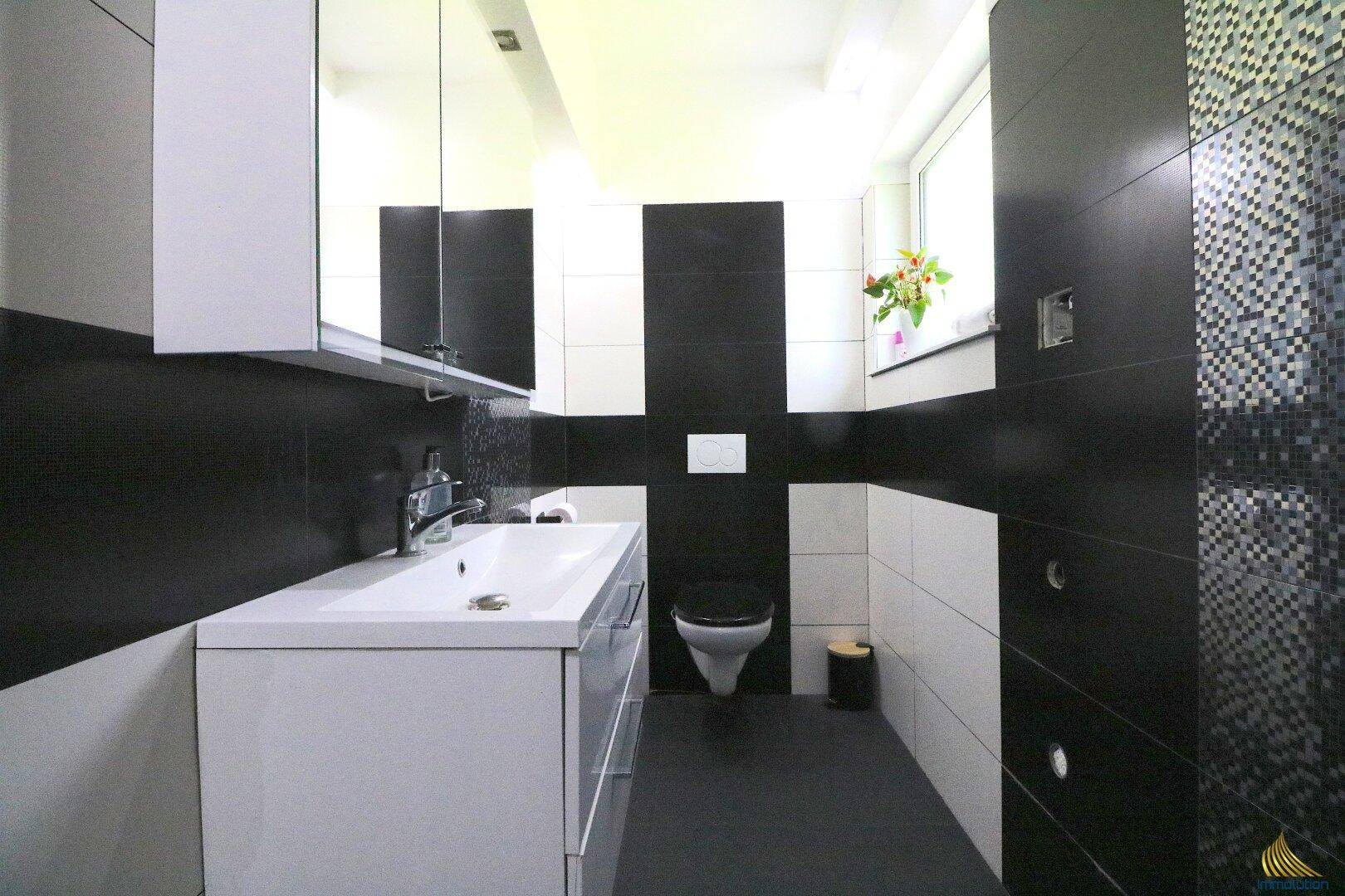 Modernes Gäste-WC mit wandhängendem WC, Einzelwaschbecken und stilvollen schwarz-weißen Fliesen.
