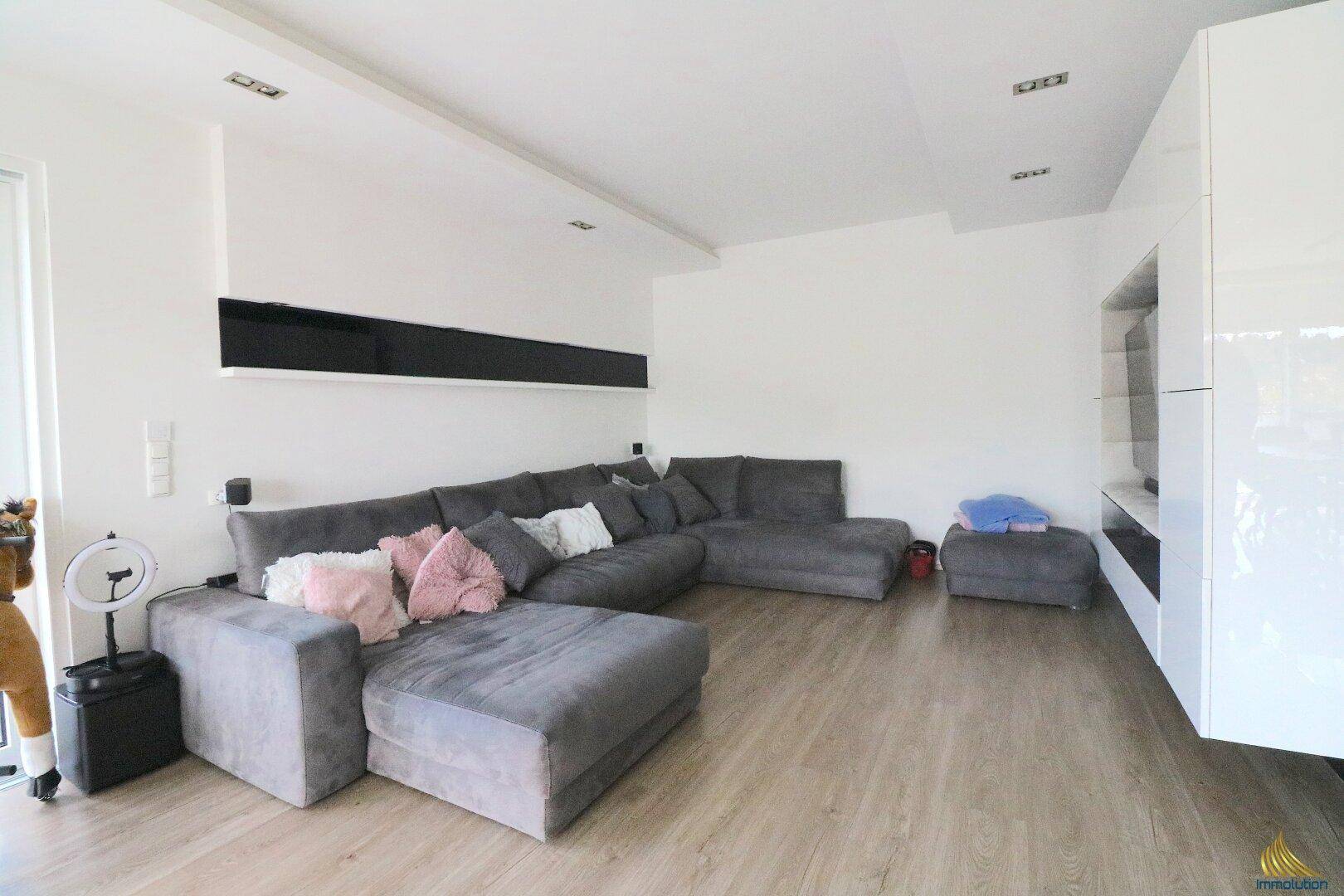 Großzügiges Wohnzimmer mit bequemer Couch, moderner Einrichtung und viel natürlichem Licht.