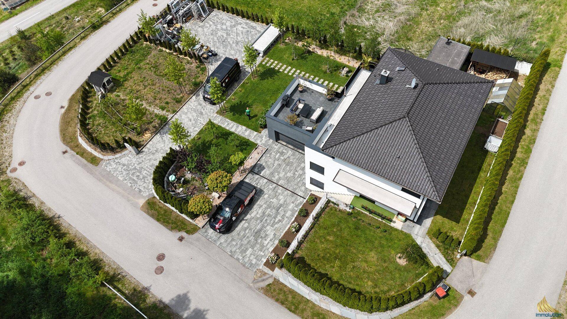 Weitläufige Luftaufnahme der modernen Villa mit großem Grundstück, gepflasterter Auffahrt und Garten.