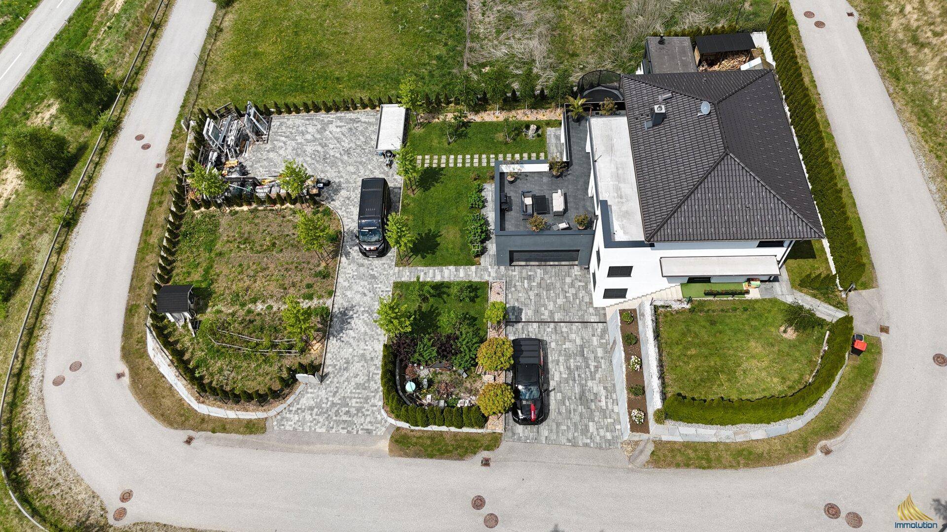 Gesamtansicht der modernen Villa von oben, umgeben von Grünflächen und mit weitläufiger Auffahrt.