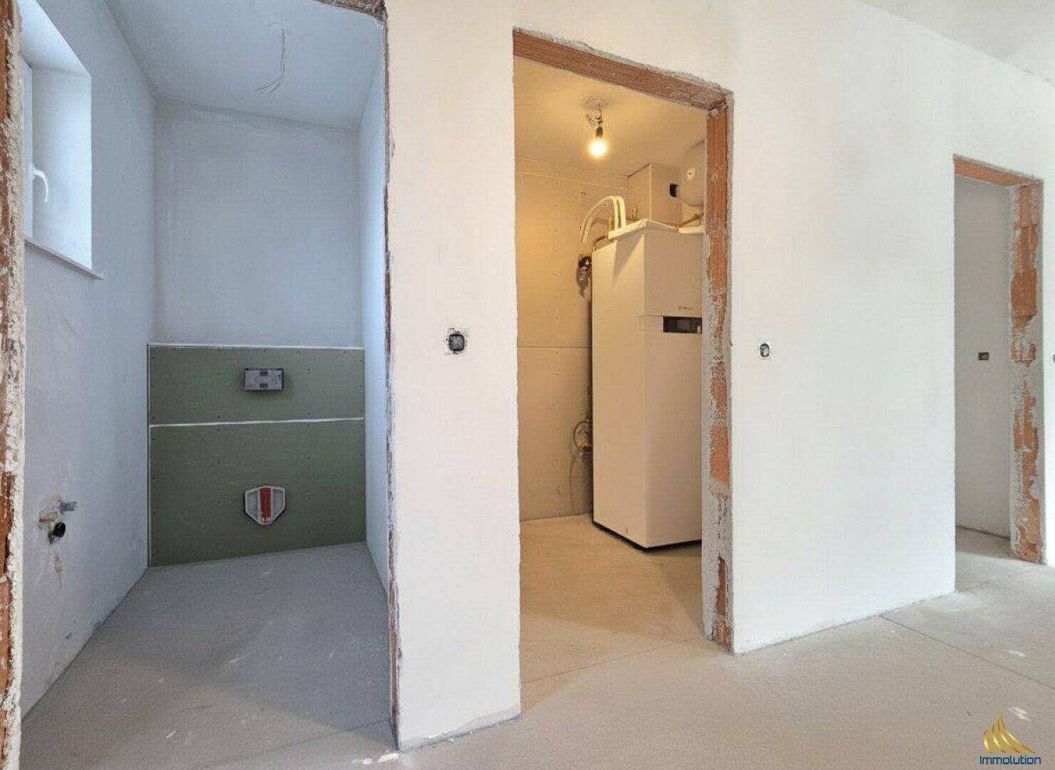 Technikraum im Rohbau mit Heizungsanlage und angrenzendem unfertigen Badezimmerbereich.