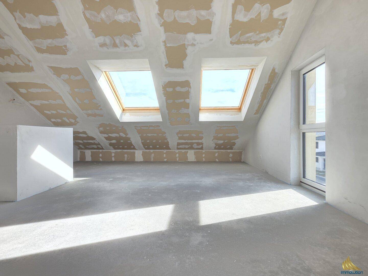 Unausgebauter Dachbodenraum mit zwei Dachfenstern und Rohbauzustand der Wände.