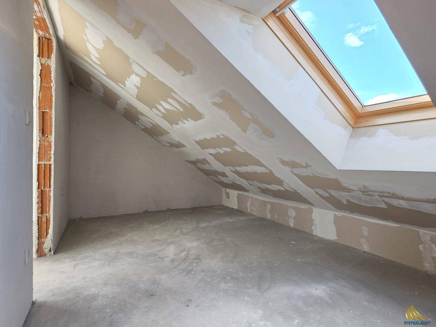 Dachbodenraum im Rohbau mit sichtbaren Ziegelwänden und einem großen Dachfenster.