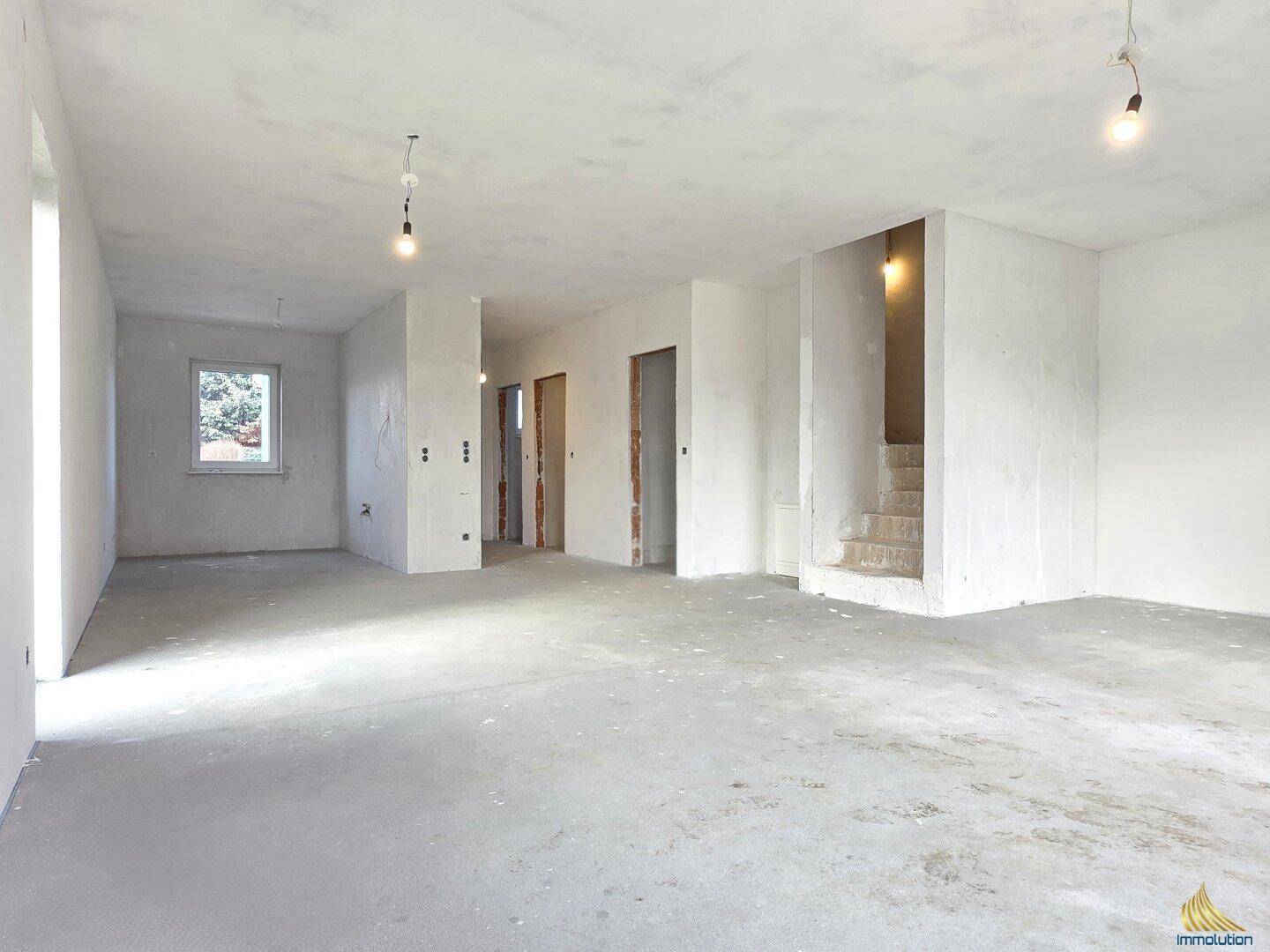 Großer offener Rohbau-Wohnbereich mit Treppenaufgang und mehreren Türöffnungen.