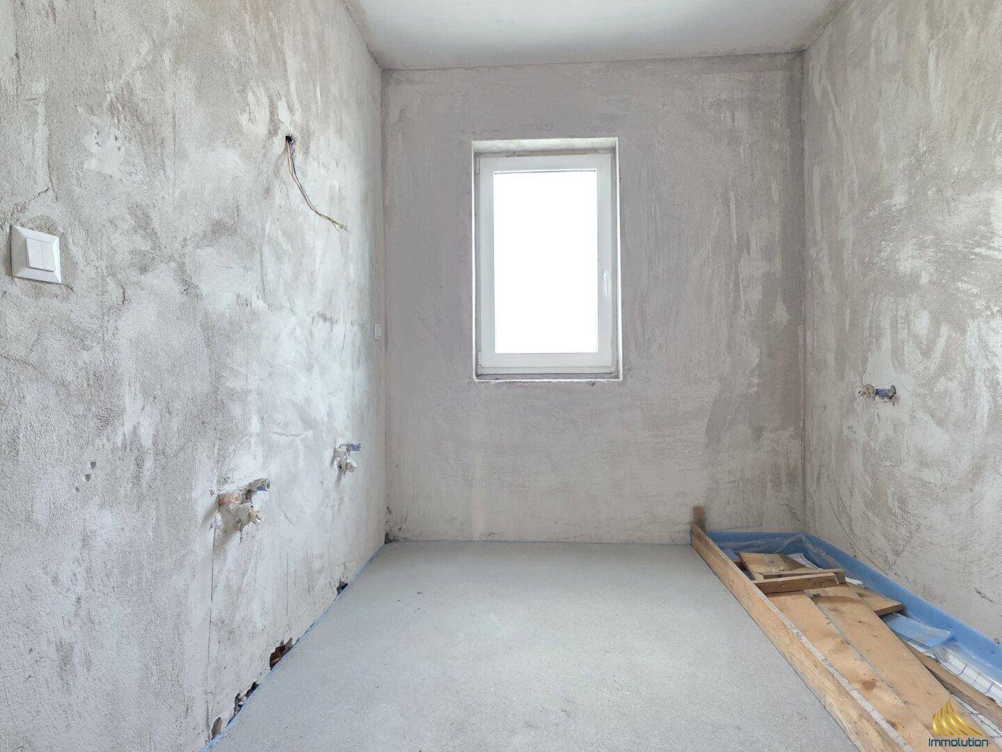 Rohbau-Badezimmer mit Fenster und vorbereiteten Anschlüssen für Sanitärinstallationen.