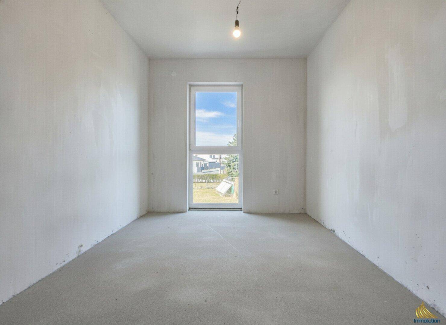 Heller Rohbau-Wohnraum mit großer Fenstertür und Blick ins Grüne.